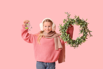 Cute girl with Christmas wreath and mini shopping cart on pink background