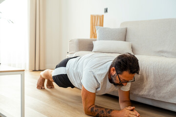 The man practices his daily workout at home on the floor, wearing casual athletic attire, concentrating on physical conditioning and achieving his weight loss target with consistency and discipline