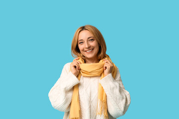 Beautiful mature woman in white sweater and stylish scarf on blue background