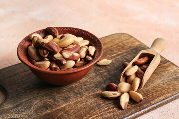 Bowl and wooden scoop with tasty Brazil nuts on beige background