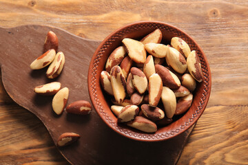 Bowl and board with tasty Brazil nuts on wooden background