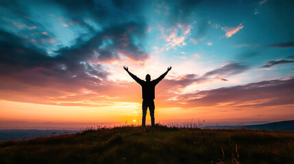 Man stands on a hill with arms raised against a vibrant sunset sky filled with dramatic clouds, capturing a moment of elevation and worship