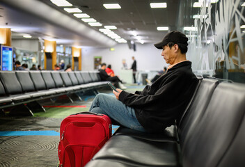 Man sitting in the airport departure area. Unrecognizable passengers and airline staff in the background.