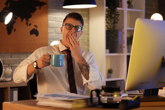 Sleepy businessman with coffee yawning in office at night