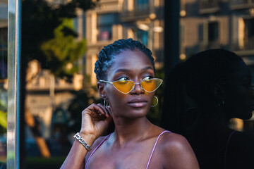 Stylish young woman in yellow sunglasses adjusting her hair and gazing off into the distance
