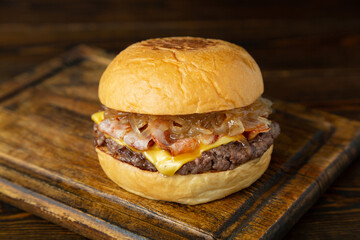 Burger, hamburger with meat patty, cheese, bacon and fried onions on a wooden board on a wooden table.