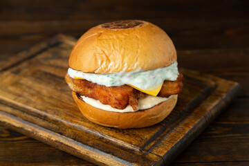 Burger, hamburger with breaded meat, cheese and white sauce on a wooden board on a wooden table.