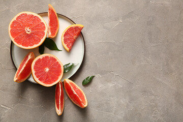 Plate with cut fresh grapefruits and leaves on grey background