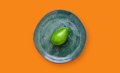 Top view of an avocado on a plate on an orange background. Healthy eating and vegetarian concept idea with fruit.