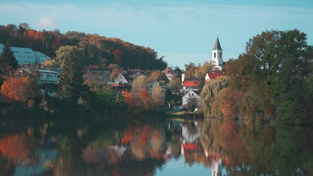St. Sebastian's and Fabian's Church in Prague sits by a calm lake, with autumn trees and houses reflected in the water.