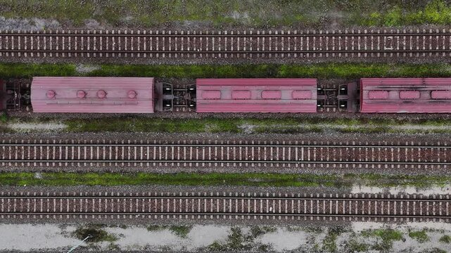 Top-down view of a red freight train moving along tracks lined with green grass