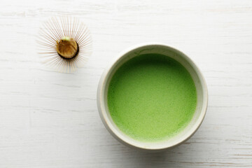 Cup of fresh matcha tea on white wooden table.