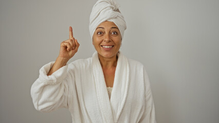 Woman smiling while pointing up wearing bathrobe with towel on head isolated on white background