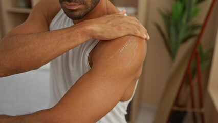 Handsome young hispanic man applies lotion to his shoulder in a serene wellness spa room