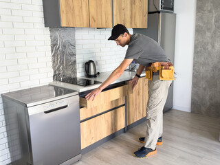 The carpenter finalizing the assembly of the kitchen shelf on the wall.
