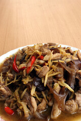 Chicken stir fry with ginger comprised of mushrooms, garlic, fresh peppers placed on a plate and on a wooden background. 