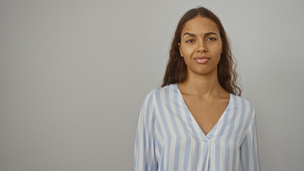 Fototapeta premium Young woman with a serious expression stands against a plain white background in a studio setting, highlighting her beauty and elegance in a striped shirt