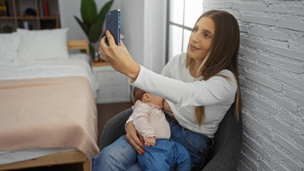 Woman taking selfie with baby in modern bedroom, showcasing motherly love and intimate family moments in a cozy home setting with natural light and relaxed atmosphere.