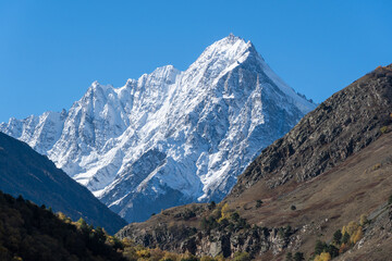 View of snow-capped peaks of Chegem Gorge. Kabardino-Balkaria. Majestic natural landscapes of Elbrus region against backdrop of blue autumn sky. Steep cliffs covered in snow and ice rise upward.