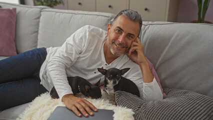 Middle-aged hispanic man relaxing indoors with two chihuahuas on a couch, showcasing a cozy home setting.