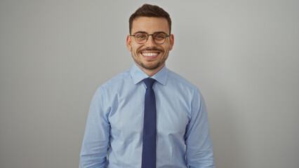 Handsome young hispanic man with a beard and glasses in a blue shirt and tie, smiling confidently against an isolated white wall background.