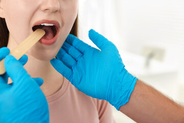 Doctor examining woman's throat with tongue depressor in clinic, closeup