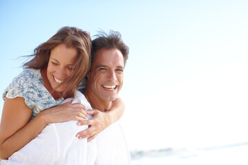 Fototapeta premium Couple, happy and piggyback on beach with love, support and playful game at sky space. Mature people, portrait and carry at ocean for travel, trust and commitment in healthy relationship in Australia