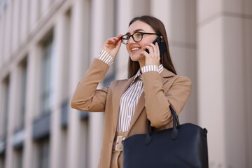 Smiling businesswoman in stylish suit talking on smartphone outdoors