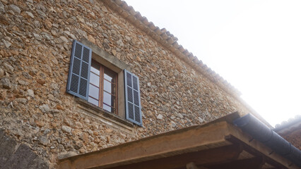 Stone building with rustic window and blue shutters showcasing mediterranean architecture under clear sky.