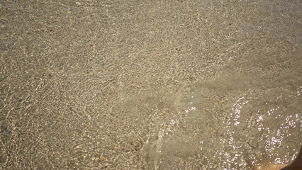 Clear water rippling at the beach shore with sunlight reflecting on the sandy seabed in an outdoor coastal setting