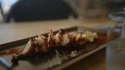 Close-up of a grilled octopus dish served on a plate at an outdoor dining setting during a sunny day.