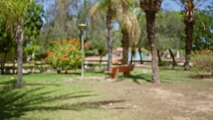 Blurred view of an outdoor park with palm trees, benches, blooming flowers, and defocused greenery under a bright blue sky