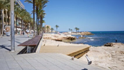 Blurred coastal promenade with palm trees, beachgoers, and a clear blue sea under a sunny sky.