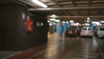 Blurred view of an out-of-focus parking garage featuring several defocused cars under bokeh lighting with a blurred fire extinguisher against the wall