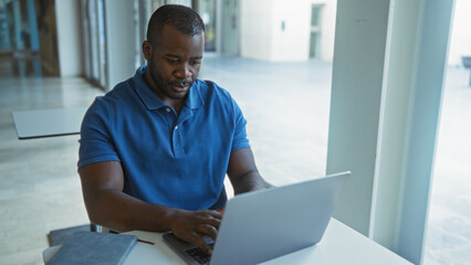 Young man working on laptop in an office setting with a focused expression on his face, suggesting a professional environment.