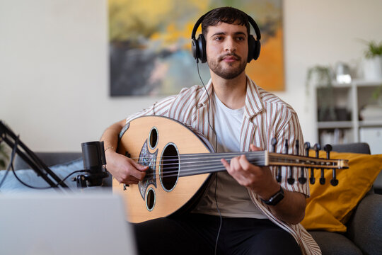 Close-up of a man wearing headphones, strumming an oud while recording in a cozy living room, capturing the essence of home music production and passion for musical creation.