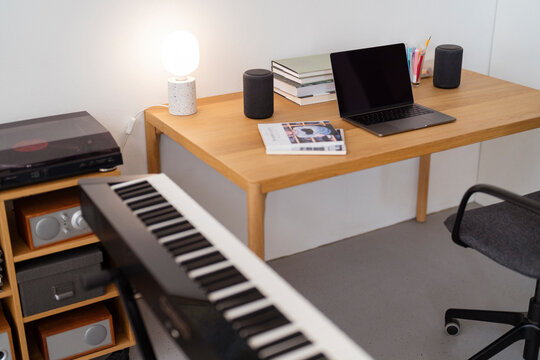 A sleek home studio desk featuring a laptop, a keyboard, speakers, and books, creating a modern and minimalist workspace ideal for productivity in a relaxed indoor environment.