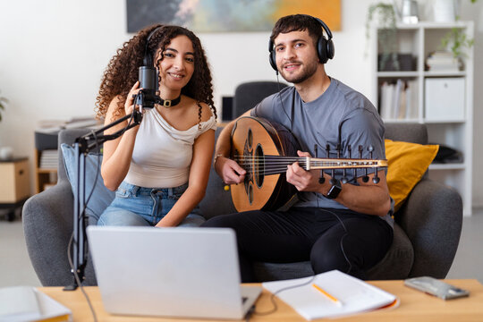 Arab young woman with a microphone and a man with an oud smile while recording music in a cozy living room, showcasing the joy and passion of a collaborative music session in a home studio.