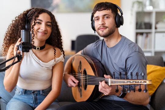 Arab young woman with a microphone and a man with an oud smile while recording music in a cozy living room, showcasing the joy and passion of a collaborative music session in a home studio.
