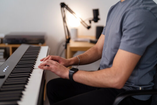 A close-up of a young man’s hands as he plays a keyboard in a home studio, highlighting his focus on the keys and the detail-oriented nature of music practice in a creative indoor setting.