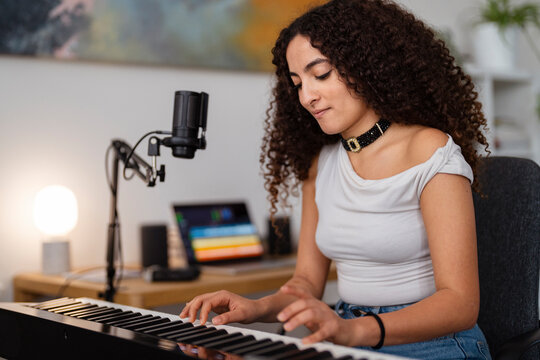 young woman is focused on her keyboard practice in a home studio, sitting by a microphone in a creative and professional setup that highlights her musical dedication and skill.