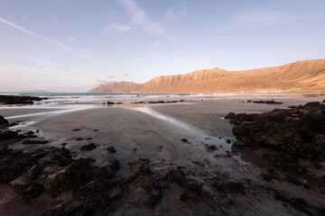 panoramic view of Famara Beach with mountains and cliff with ocean under clear sky in Teguise, Lanzarote at Canary Islands in Spain, concept of wild nature and marine landscape