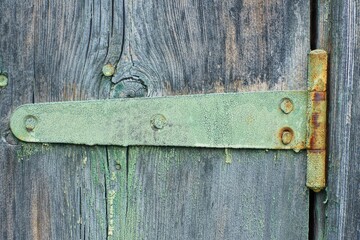 one iron heavy long  green painted rusty nailed old industrial retro gate opener hanging hanger on gray wooden board fence day outdoors	