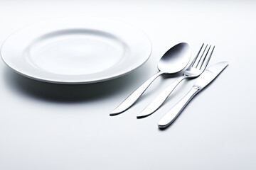 Silver colored cutlery such as spoons, forks, knives, cups and plates photographed against a white background