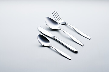 Silver colored cutlery such as spoons, forks, knives, cups and plates photographed against a white background