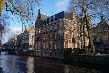 Fototapeta premium Canal reflecting the sunlight on a beautiful day with traditional brick buildings lining the water in amsterdam, netherlands