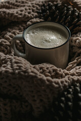 Coffee with milk in a white mug in a warm knitted blanket. Cozy still life