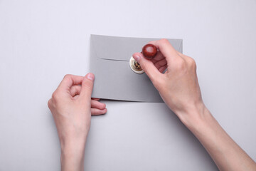 Girl sealing envelope with wax sealing stamp on gray background