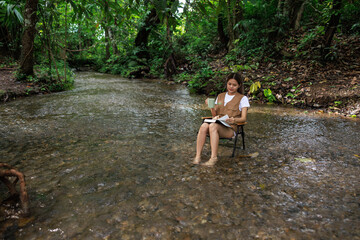 woman sitting on a chair in the stream and drinking coffee with a book in her hand