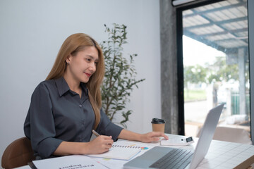 A woman is sitting at a desk with a laptop and a cup of coffee